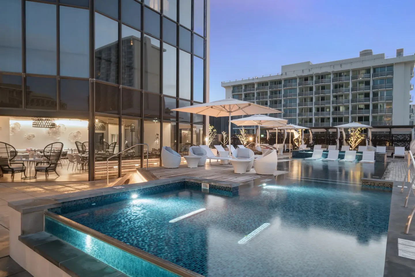 Pool deck with loungers, umbrellas and glass-front building at Hyatt Centric Waikiki Beach.
