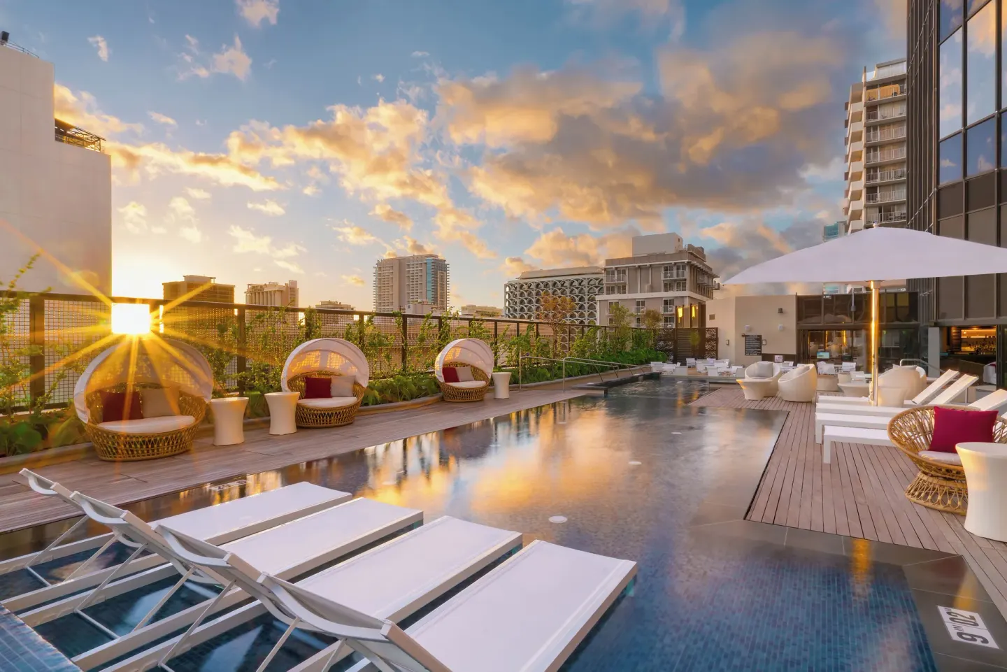 Rooftop pool deck at Hyatt Centric Waikiki Beach with lounge chairs and city views at sunset.