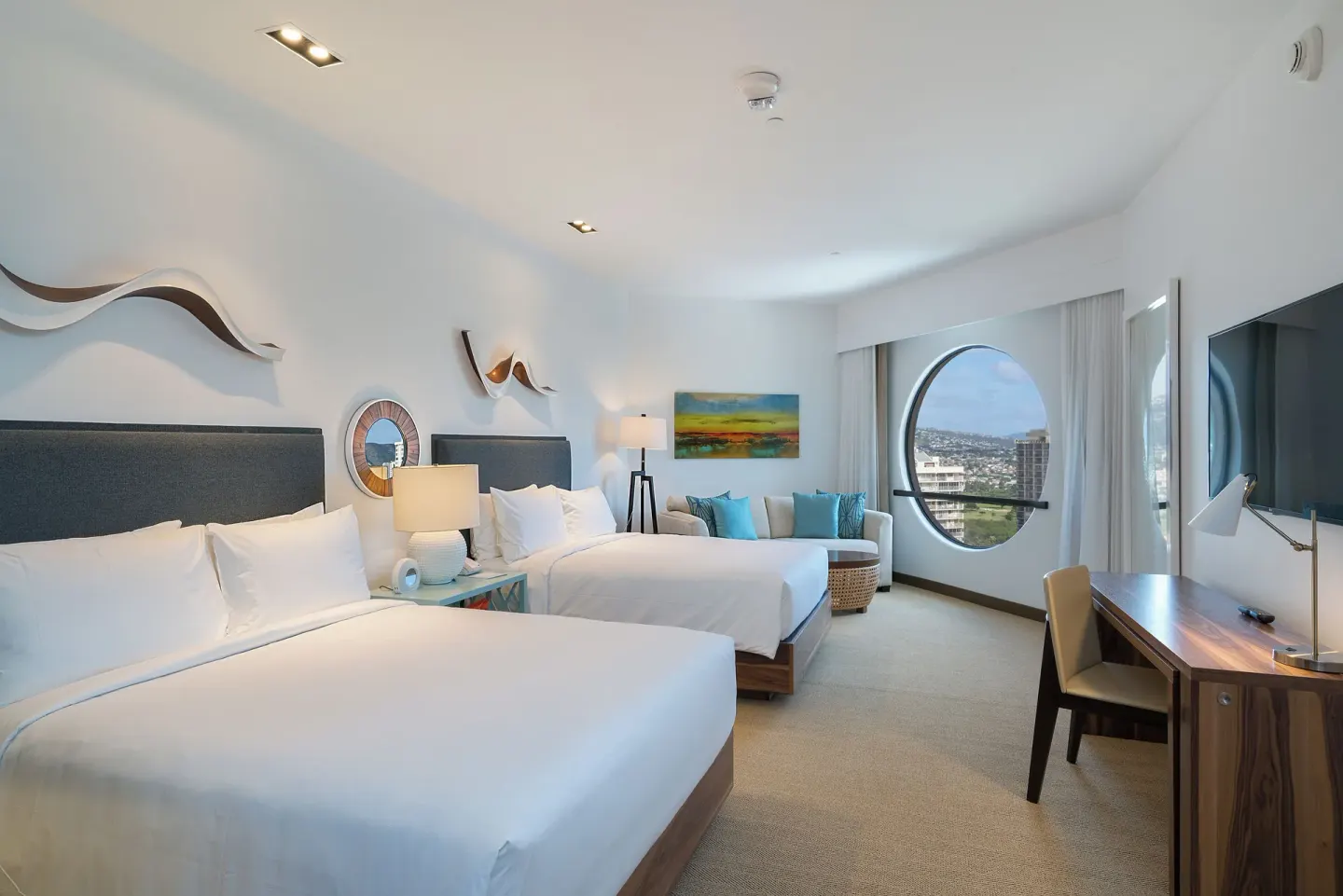Deluxe room with two beds, round window, sofa, and desk at Hyatt Centric Waikiki Beach.