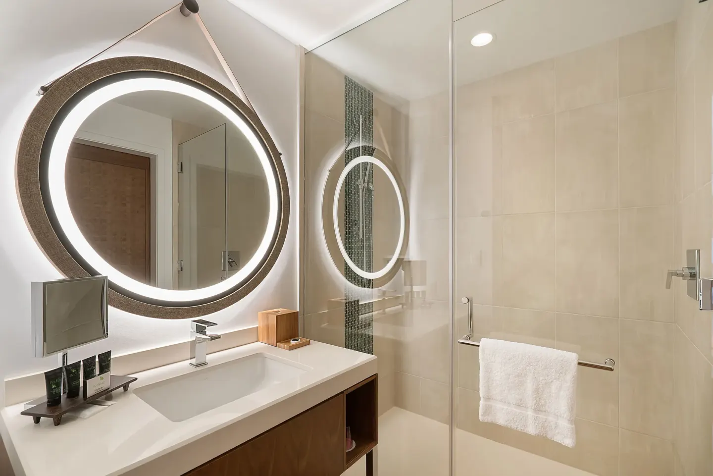 Guest room bathroom with lit round mirror and glass shower at Hyatt Centric Waikiki Beach.