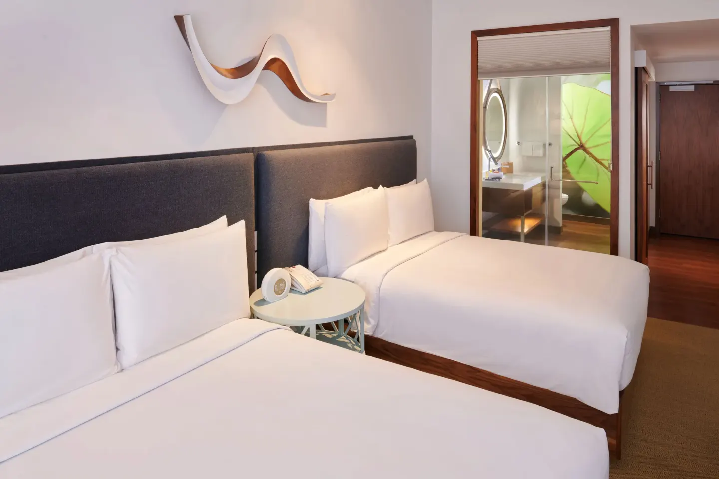 Two white beds in a guest room at Hyatt Centric Waikiki Beach with bathroom visible beyond.