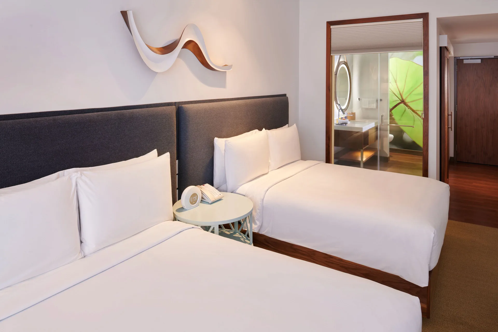 Two white beds in a guest room at Hyatt Centric Waikiki Beach with bathroom visible beyond.