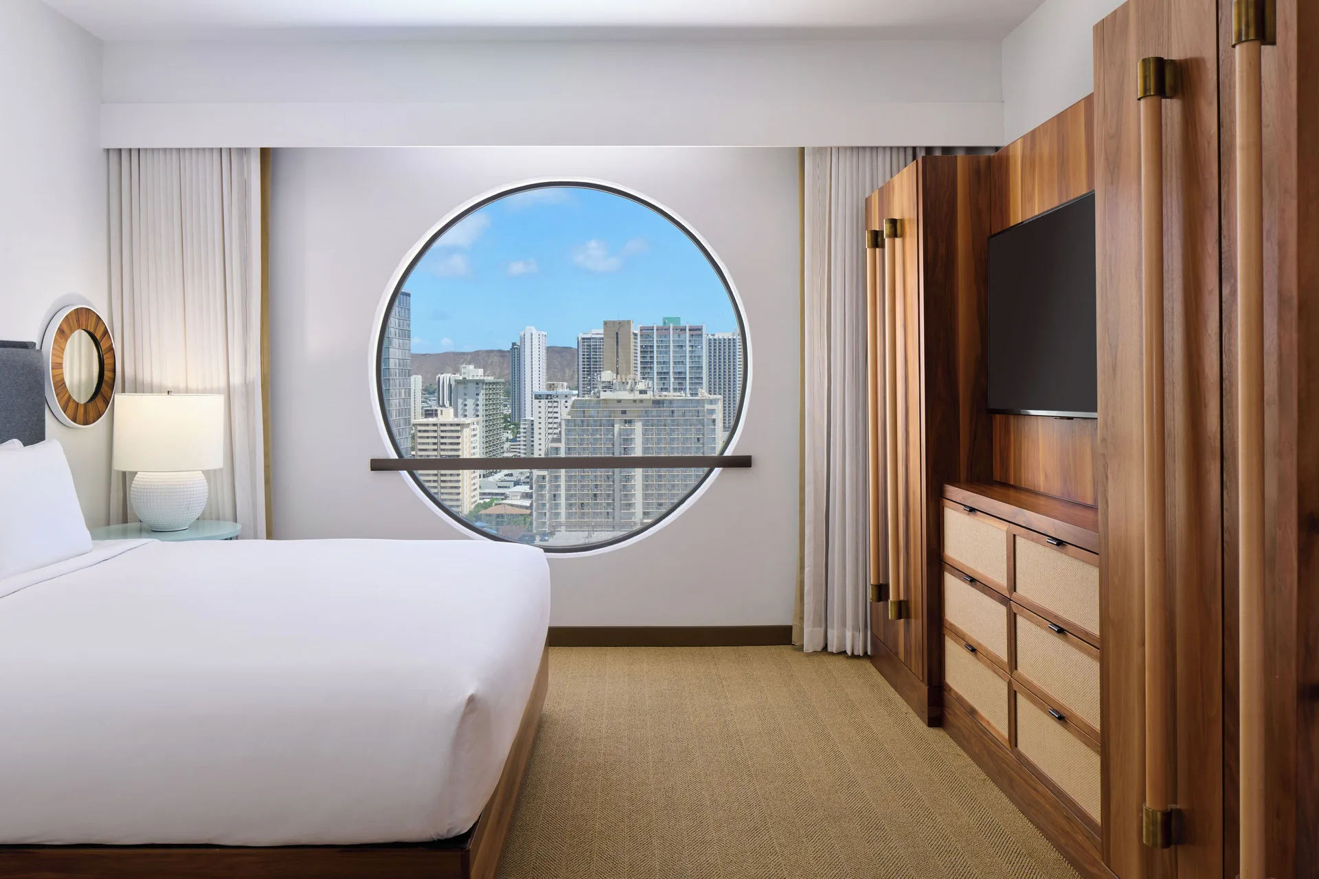 Suite Ocean View at Hyatt Centric Waikiki Beach with king bed, modern bedroom décor, and round window showcasing Pacific Ocean views in Honolulu.