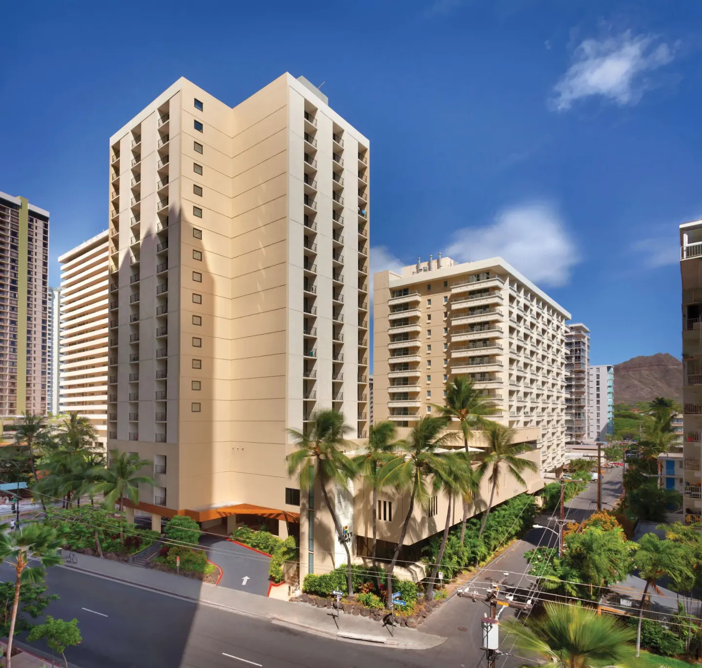 Exterior towers of Hyatt Place Waikiki Beach with balconies, palms, and city streets below.