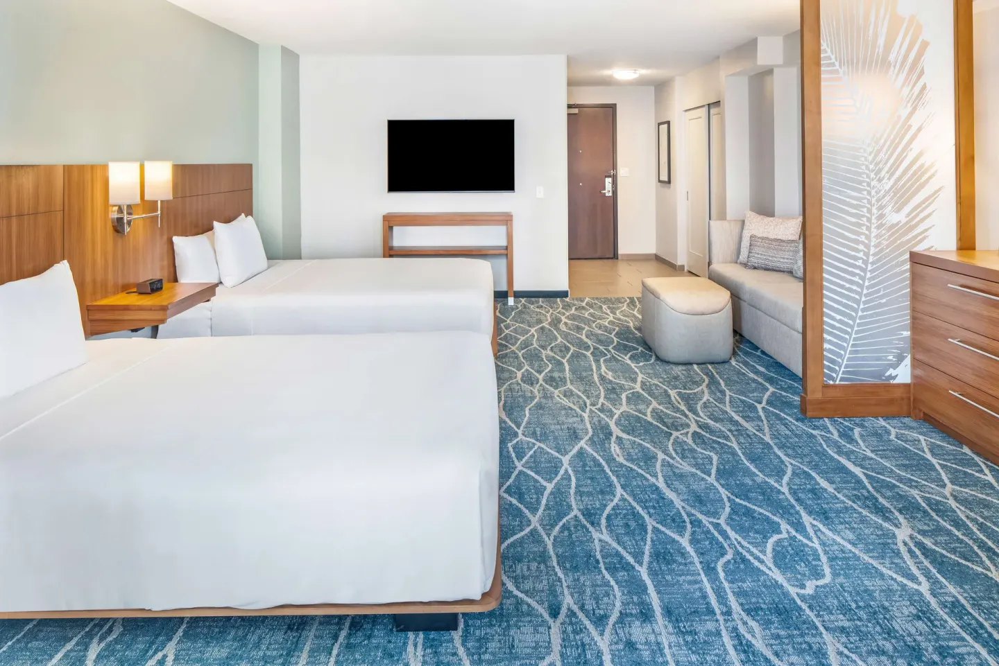 Guest room with two beds, sofa, ottoman, and wall-mounted TV at Hyatt Place Waikiki Beach.