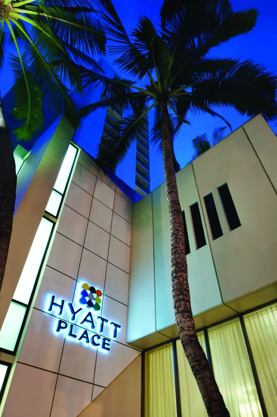 Illuminated exterior sign and palm trees at Hyatt Place Waikiki Beach.