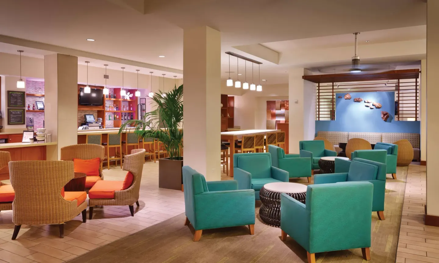 Lobby lounge with teal chairs, wicker seating, and bar area at Hyatt Place Waikiki Beach.