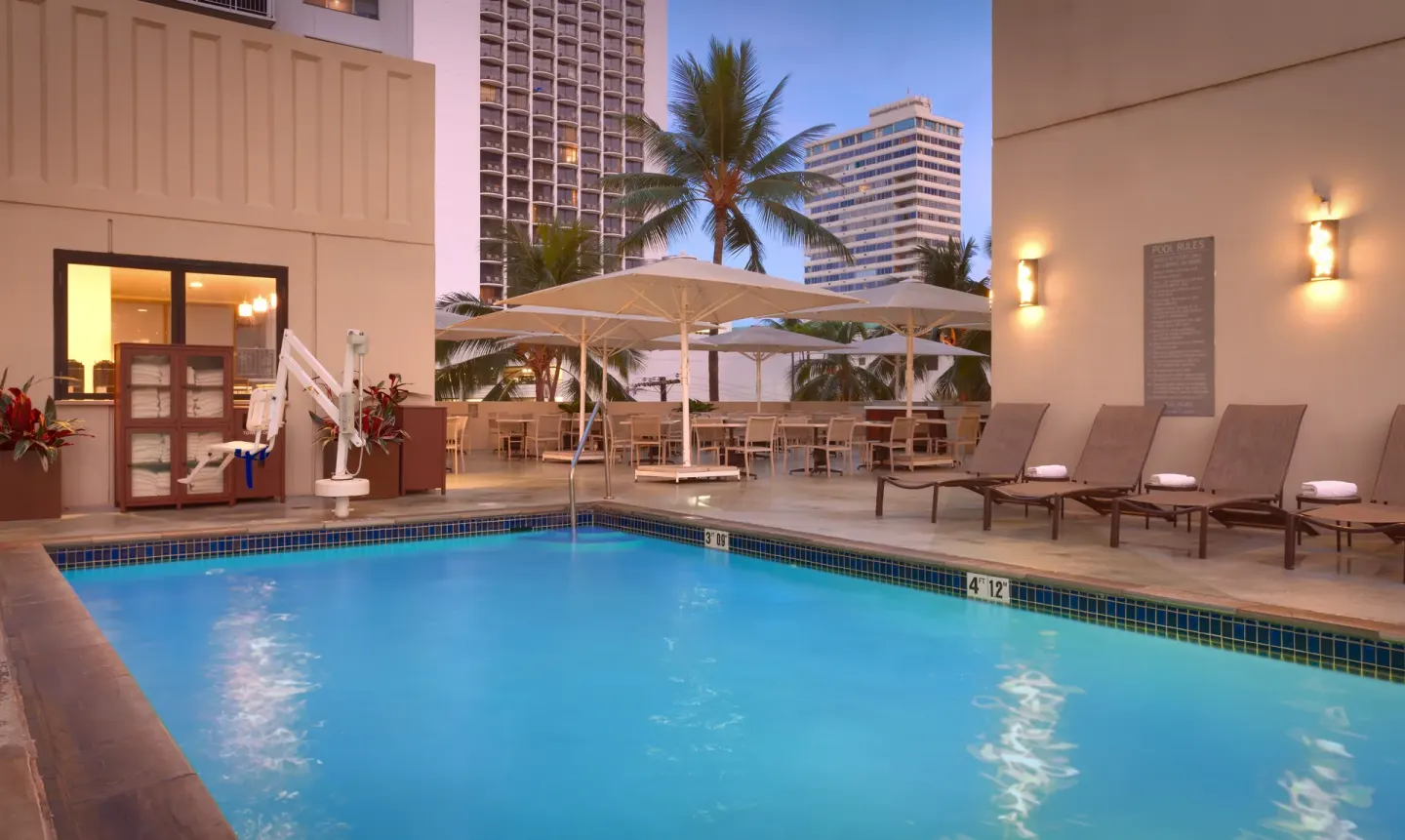 Outdoor pool with lounge chairs, umbrellas, and city buildings at Hyatt Place Waikiki Beach.