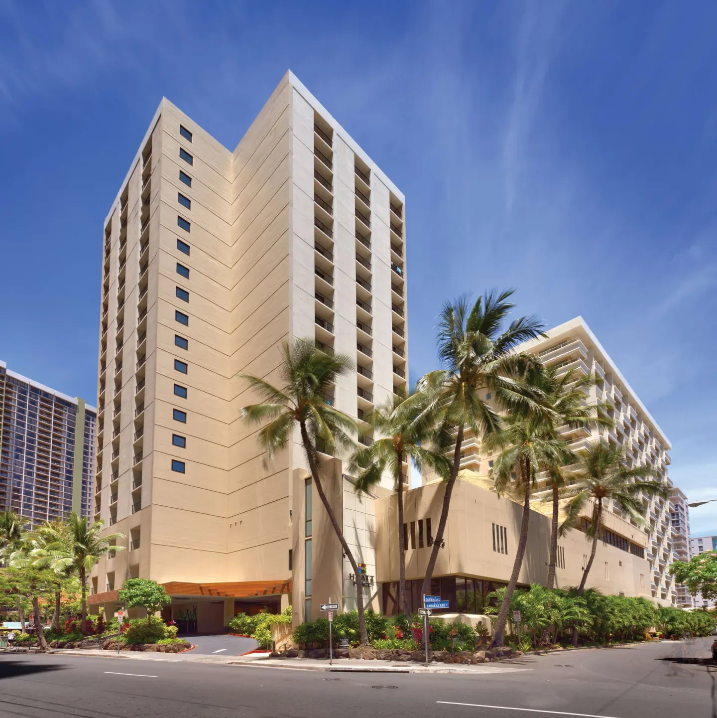 Street-level exterior of Hyatt Place Waikiki Beach with palms and tall hotel towers.