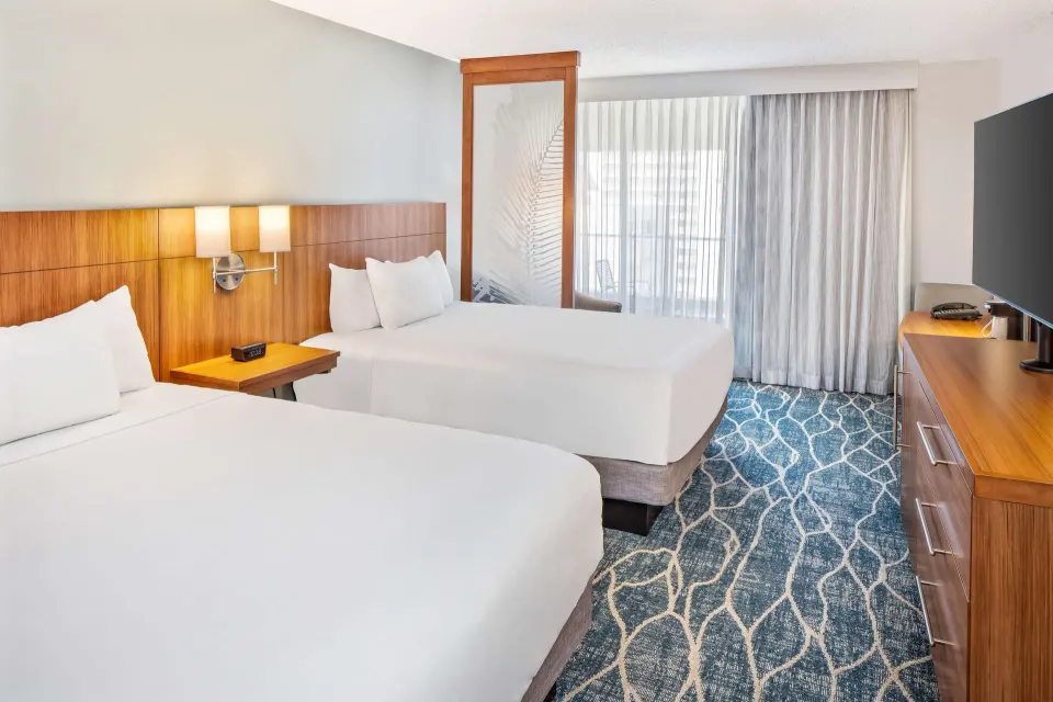 Two queen beds in an ocean view room at Hyatt Place Waikiki Beach with balcony curtains and TV dresser.