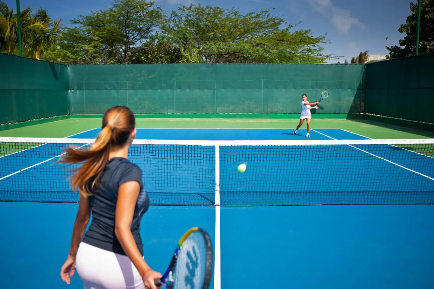 Two guests playing tennis on a blue court at Hyatt Regency Aruba Resort and Casino.