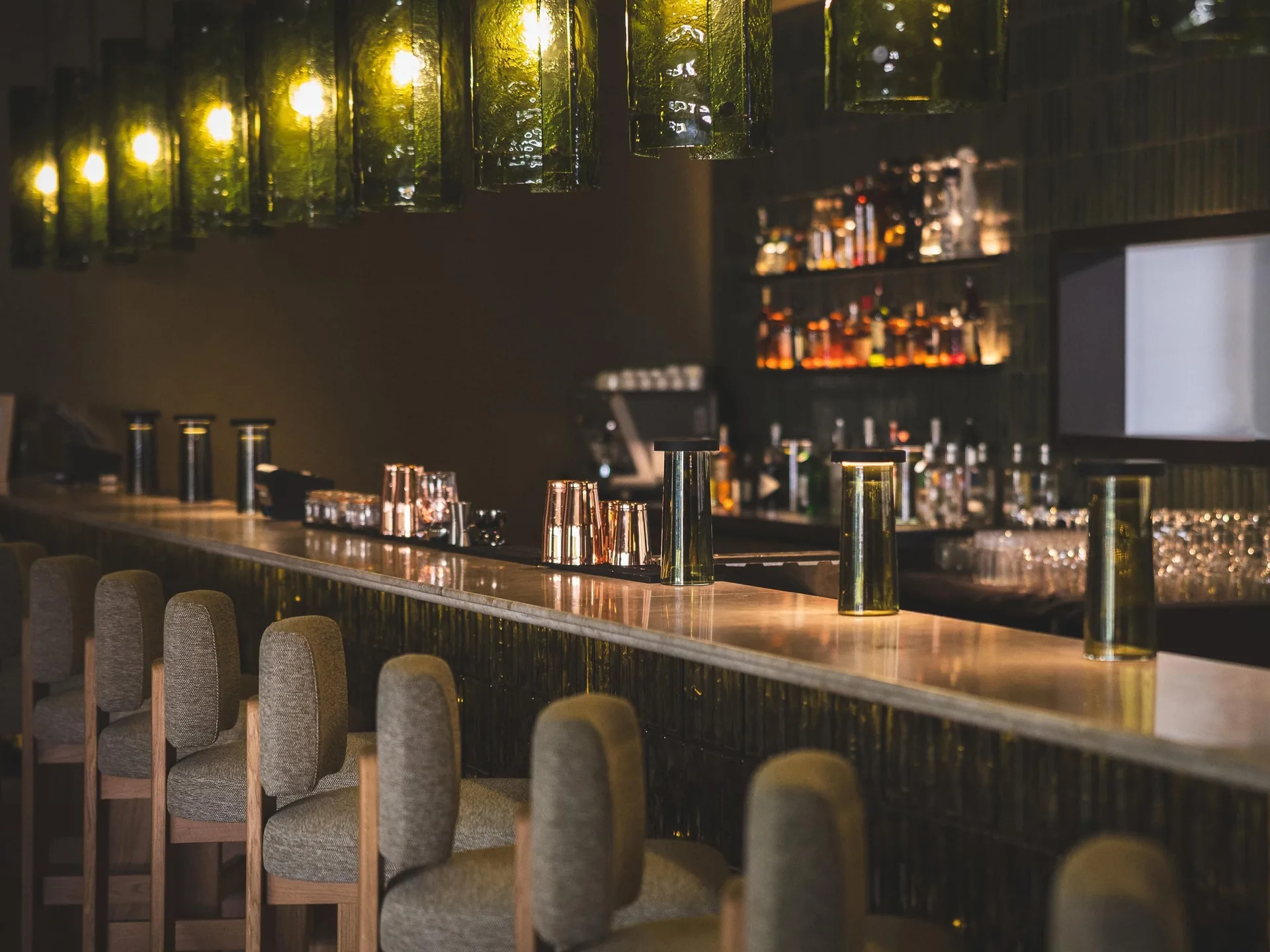 Polished bar with cushioned stools and glowing green pendant lights at Hyatt Regency Aruba Resort and Casino.