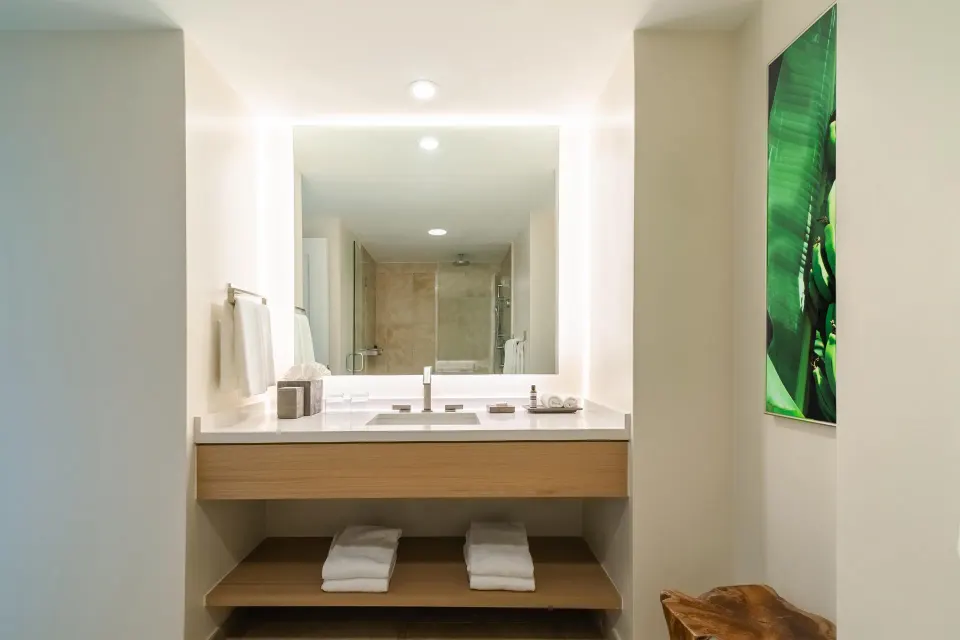 Guest bathroom vanity with lit mirror and shower reflection at Hyatt Regency Aruba Resort and Casino.