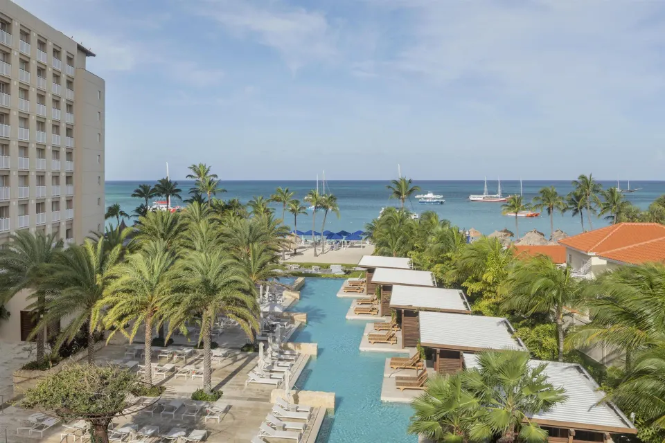 Resort view with pool cabanas, palms, beach, and ocean at Hyatt Regency Aruba Resort and Casino.