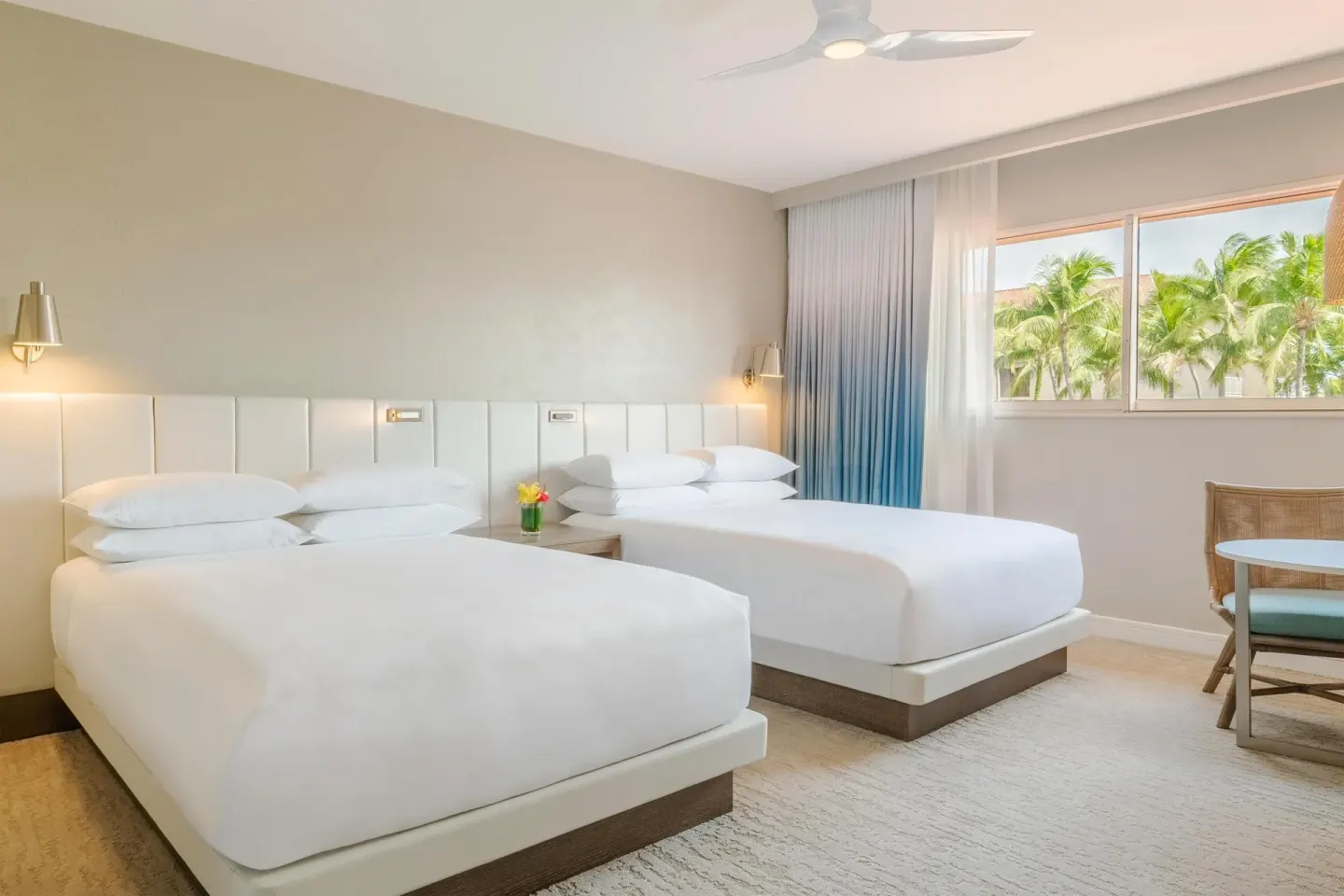 Two white queen beds in a guest room at Hyatt Regency Aruba Resort and Casino with palms outside the window.