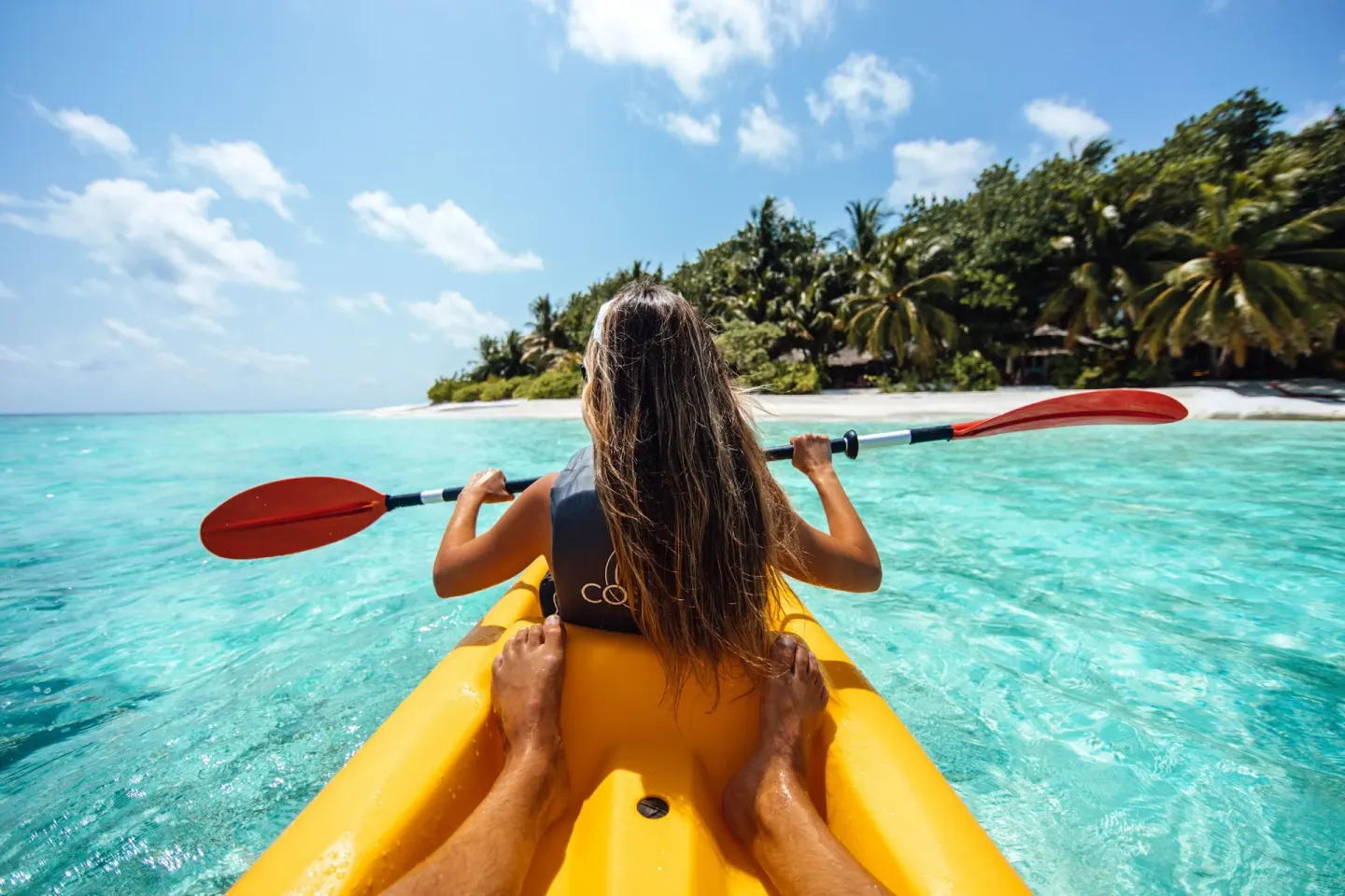 Two people kayak over turquoise water near a palm-lined beach at Hyatt Regency Grand Reserve Puerto Rico.