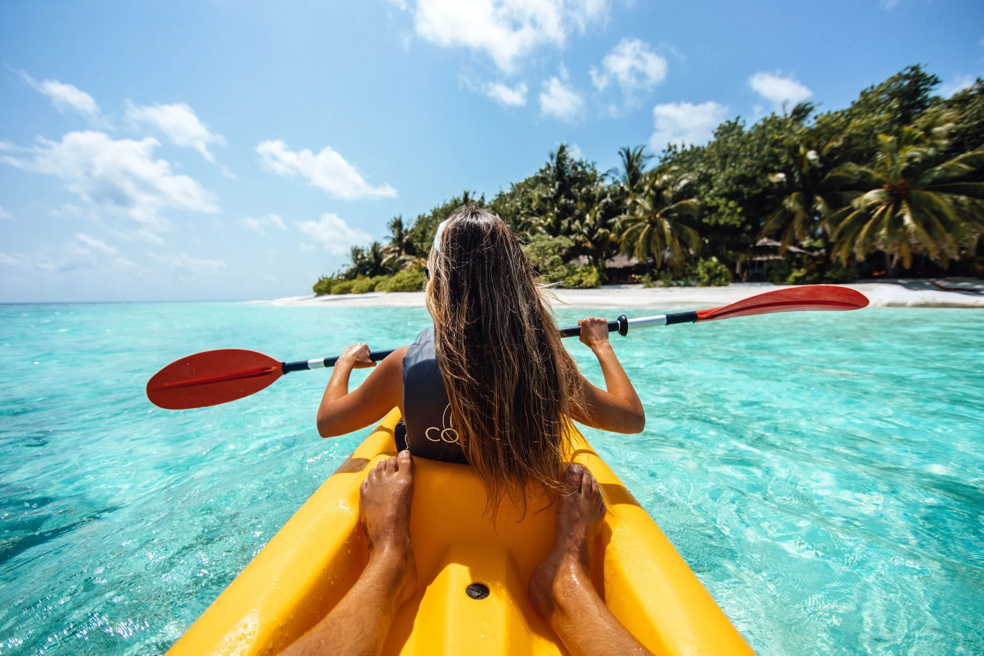 Two people kayak over turquoise water near a palm-lined beach at Hyatt Regency Grand Reserve Puerto Rico.