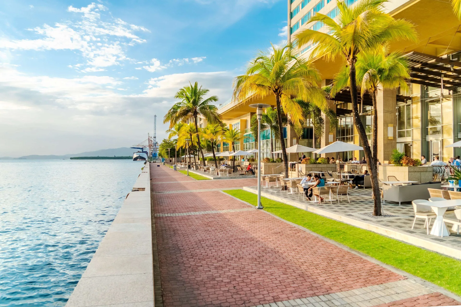 Waterfront promenade with palm trees and outdoor seating at Hyatt Regency Trinidad.