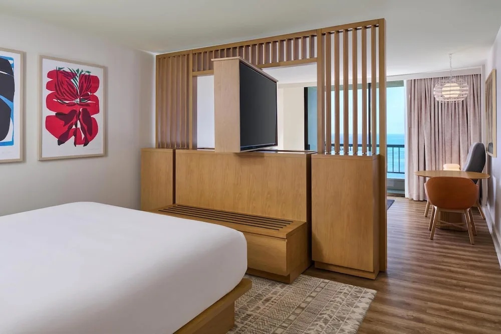Guest room with king bed, TV partition, and ocean-view balcony at Hyatt Regency Waikiki Beach Resort & Spa.