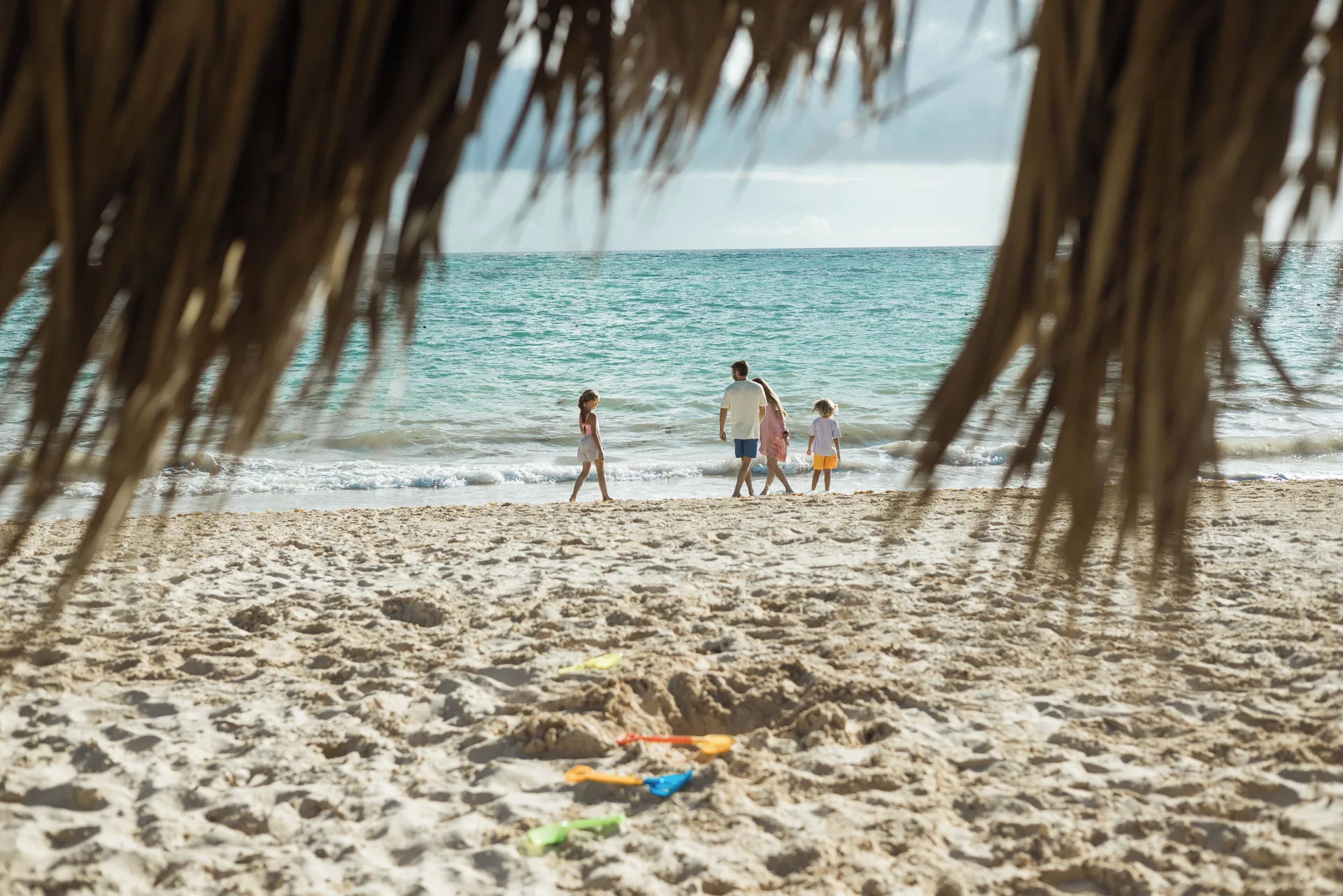 Family walks along the beach under a thatched shade at Iberostar Selection Bávaro Suites.