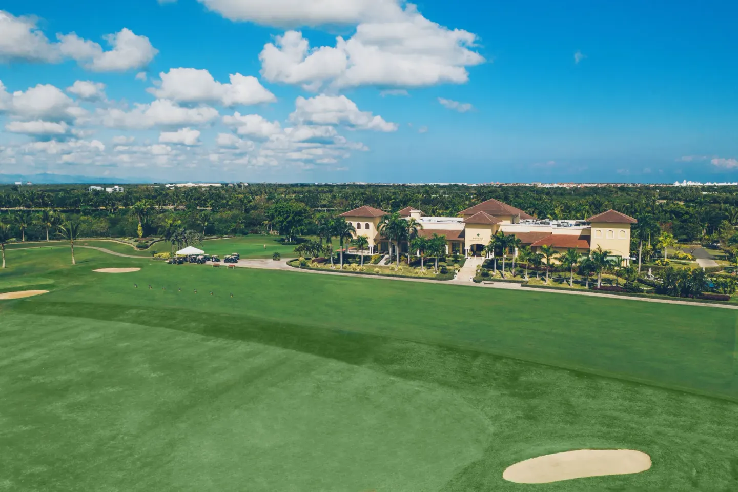 Aerial view of a golf course beside Iberostar Selection Bávaro Suites under a bright blue sky.