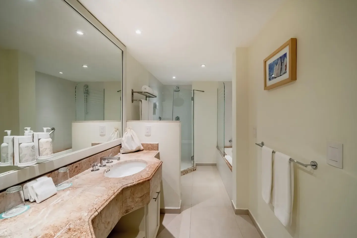 Bathroom vanity with large mirror, sink, towels, shower, and bathtub at Iberostar Selection Cancún.