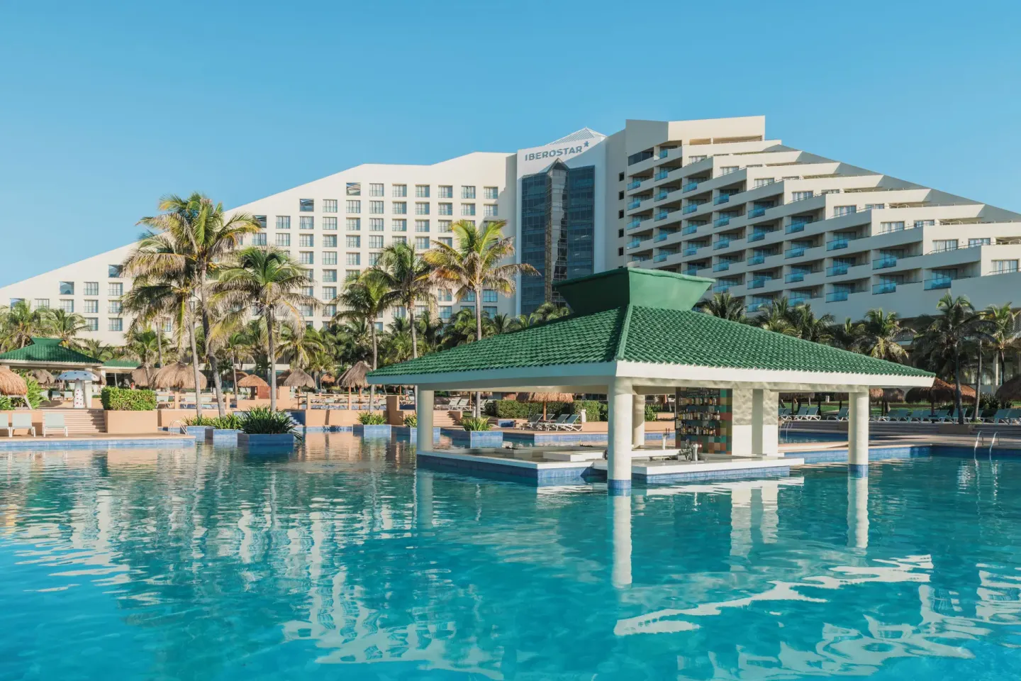 Main pool with a green-roofed swim-up bar and hotel tower at Iberostar Selection Cancún.