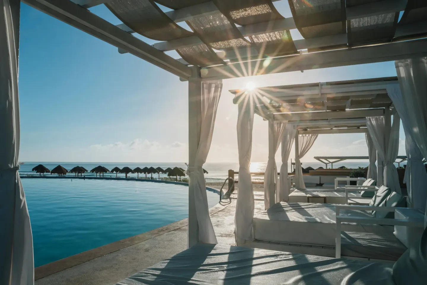 Poolside cabanas beside the ocean at sunset at Iberostar Selection Cancún.