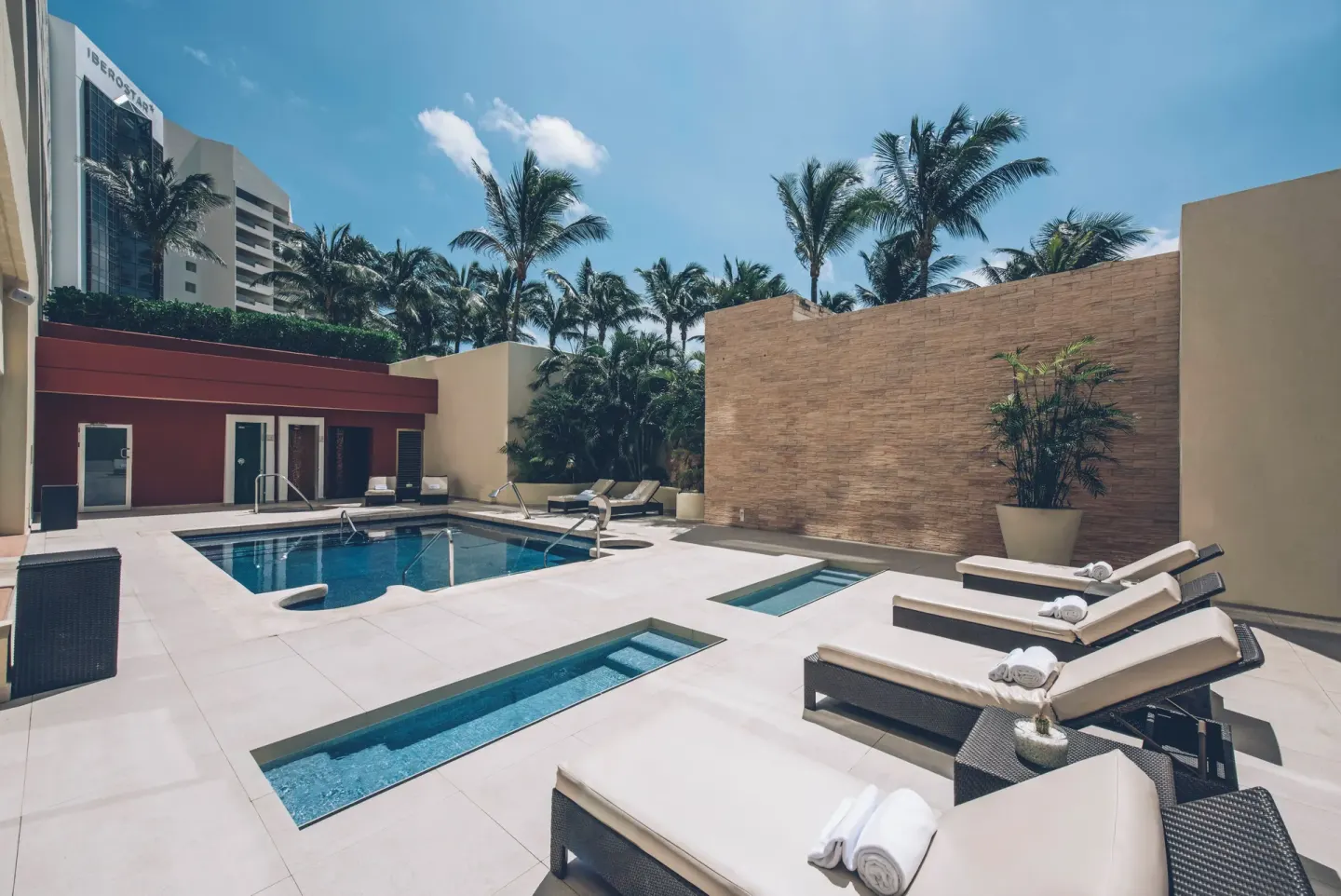 Sunlit pool terrace with loungers and palm trees at Iberostar Selection Cancún.