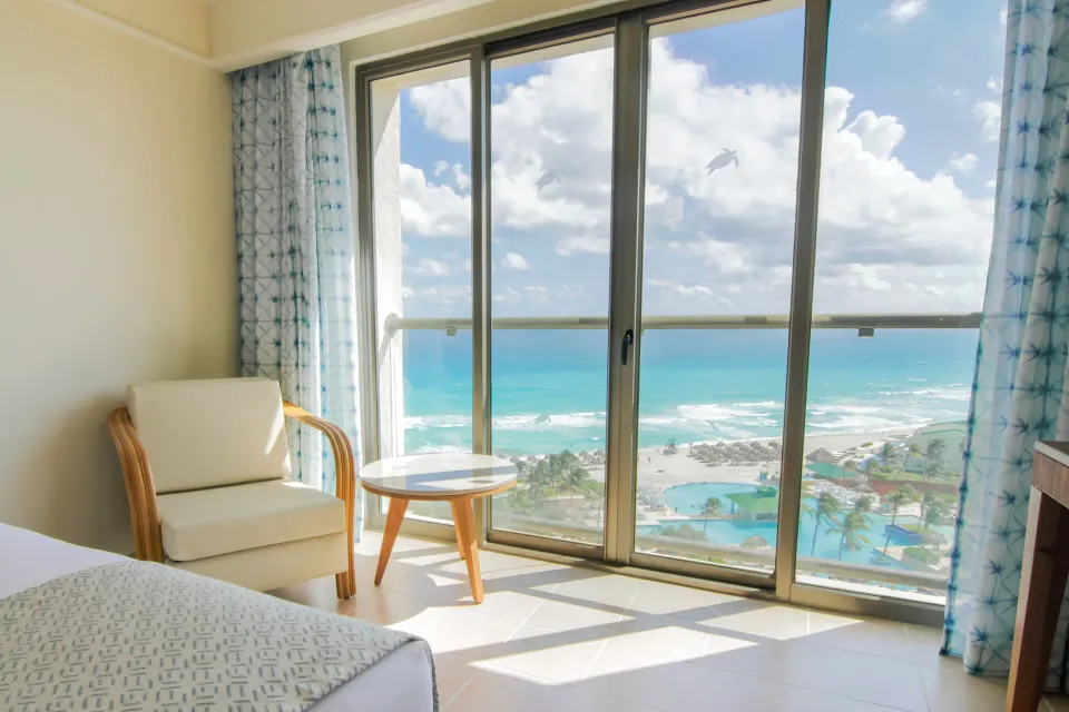 Premium Room Ocean View at Iberostar Selection Cancún with bed, chair, table, and sea-facing glass doors.