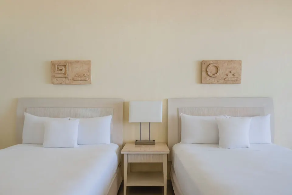 Two white beds with a shared nightstand in a villa room at Iberostar Selection Cancún.