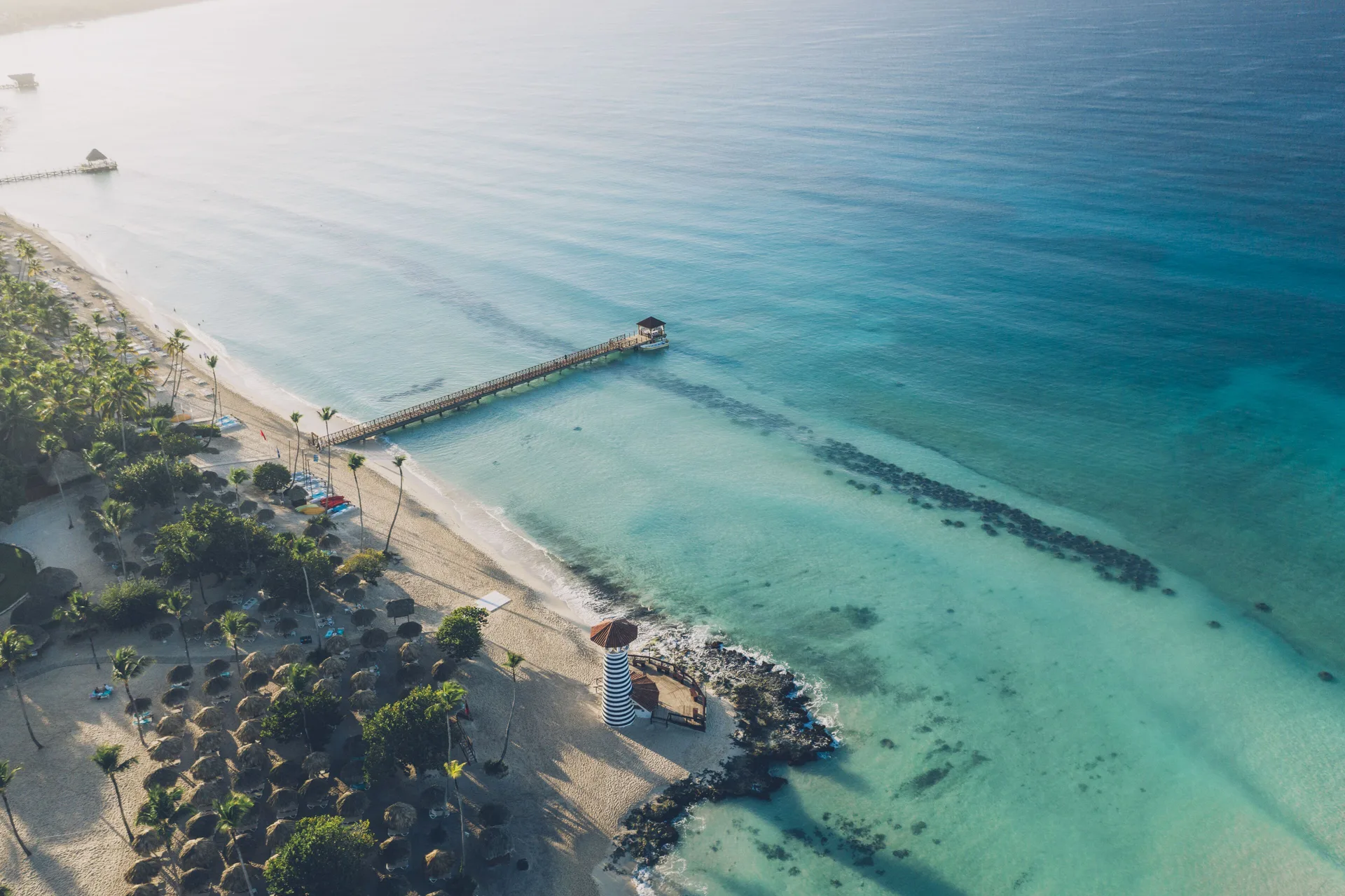 Aerial beach view with pier and striped lighthouse at Iberostar Selection Hacienda Dominicus.