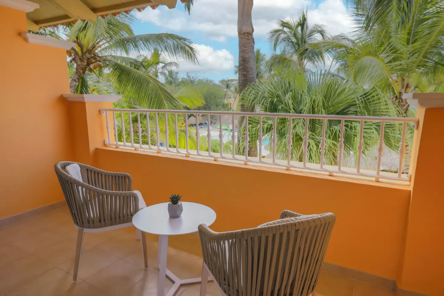 Orange balcony with two chairs and palm-filled view at Iberostar Selection Hacienda Dominicus.