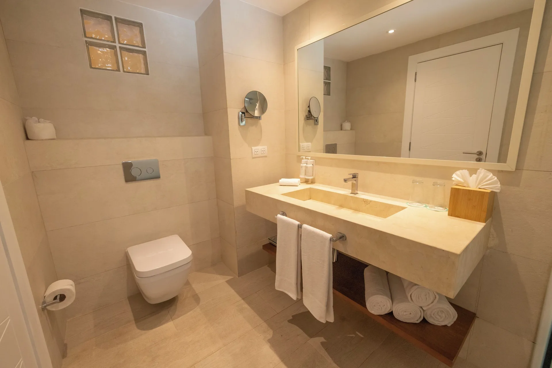 Guest bathroom with beige tile, vanity, and wall mirror at Iberostar Selection Hacienda Dominicus.