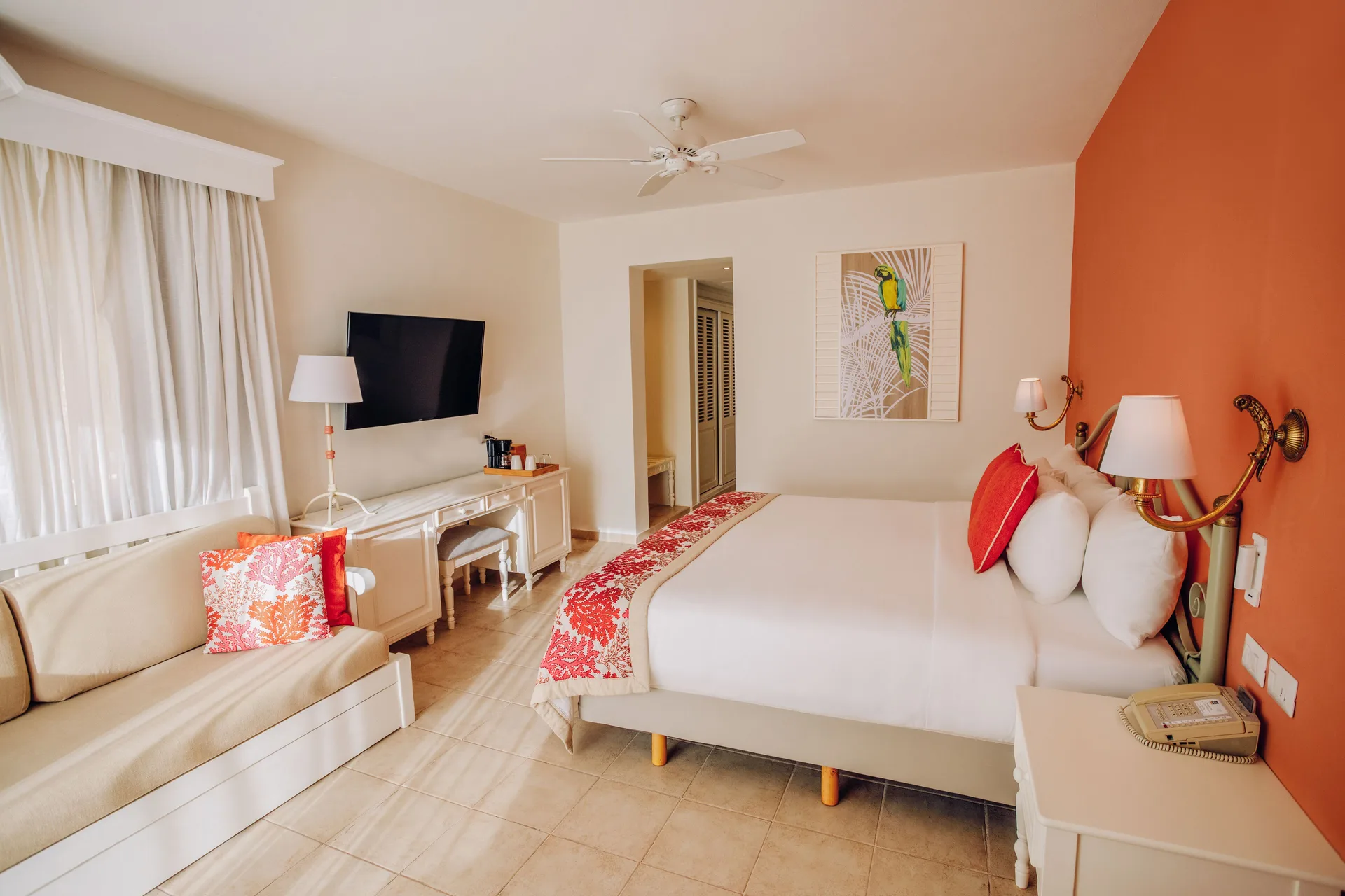Guest room with king bed, sofa, and orange accent wall at Iberostar Selection Hacienda Dominicus.
