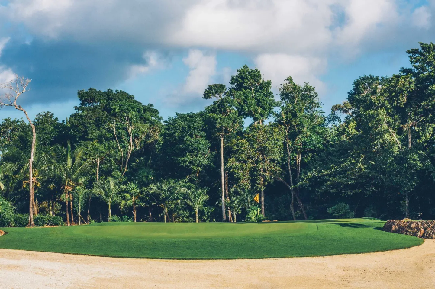 Golf green bordered by sand and dense trees near Iberostar Selection Paraíso Maya Suites.