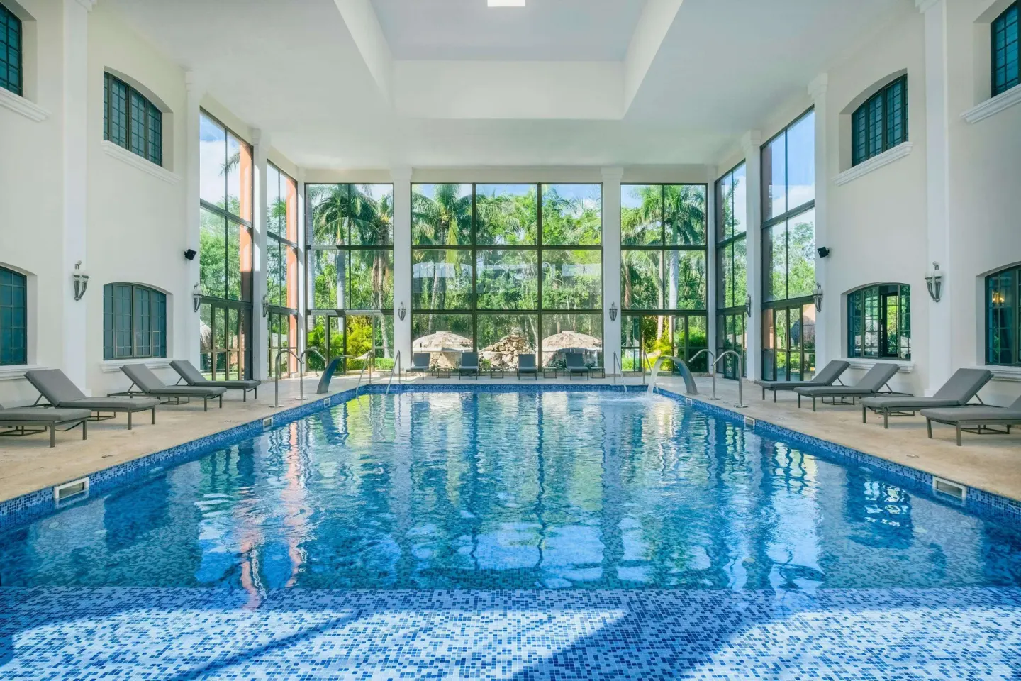 Indoor pool with lounge chairs and tall windows at Iberostar Selection Paraíso Maya Suites.