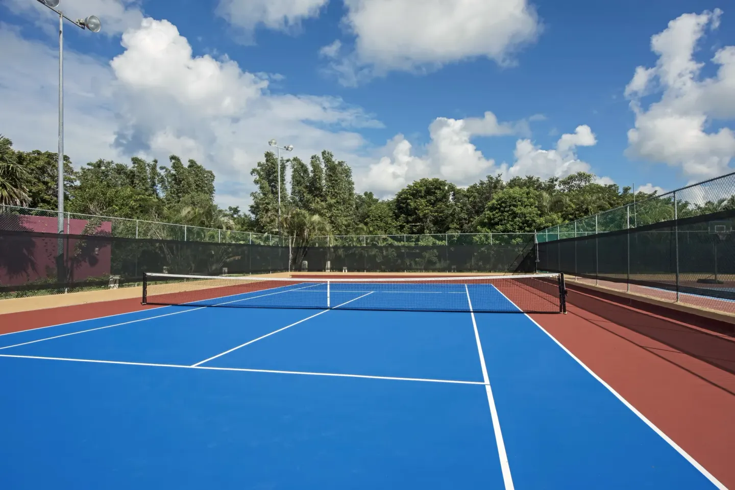 Outdoor tennis court with blue playing surface at Iberostar Selection Paraíso Maya Suites.
