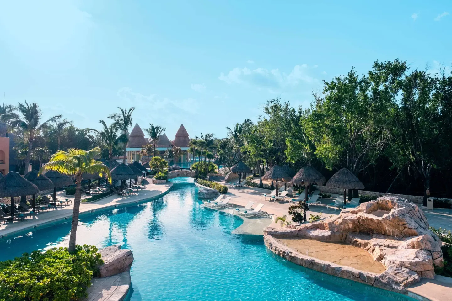 Long pool channel with palapas and rock features at Iberostar Selection Paraíso Maya Suites.