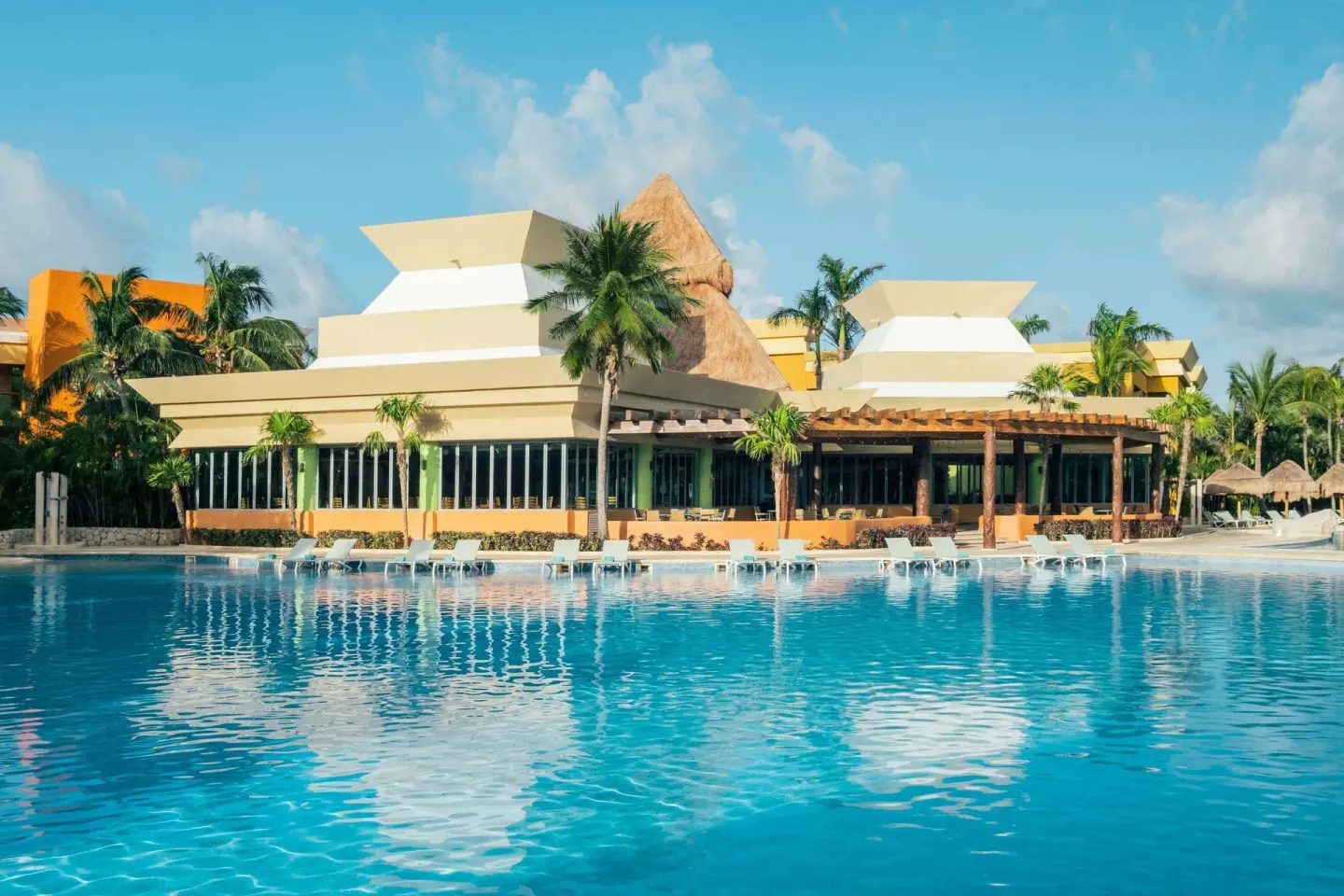 Poolside building and loungers reflected in the water at Iberostar Selection Paraíso Maya Suites.