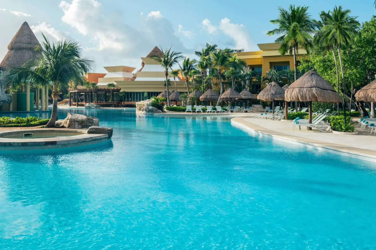 Curving pool with palapas and palms at Iberostar Selection Paraíso Maya Suites.
