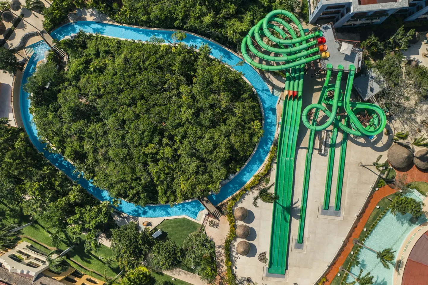 Aerial view of green waterslides beside a winding pool at Iberostar Selection Paraíso Maya Suites.