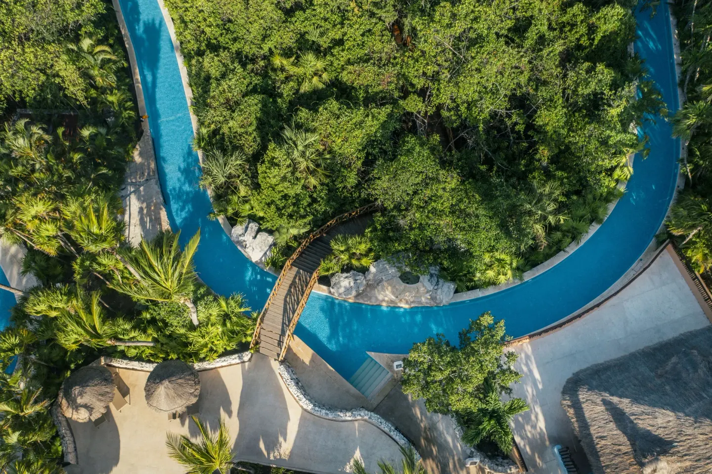 Aerial view of a winding pool and footbridge at Iberostar Selection Paraíso Maya Suites.