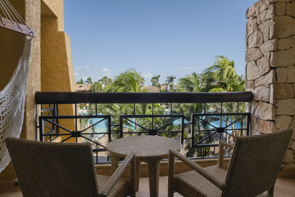 Junior Suite balcony with wicker seating and pool view at Iberostar Selection Paraíso Maya Suites.