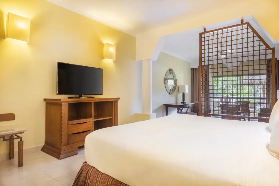 Junior Suite bedroom with king bed, TV, and balcony beyond at Iberostar Selection Paraíso Maya Suites.
