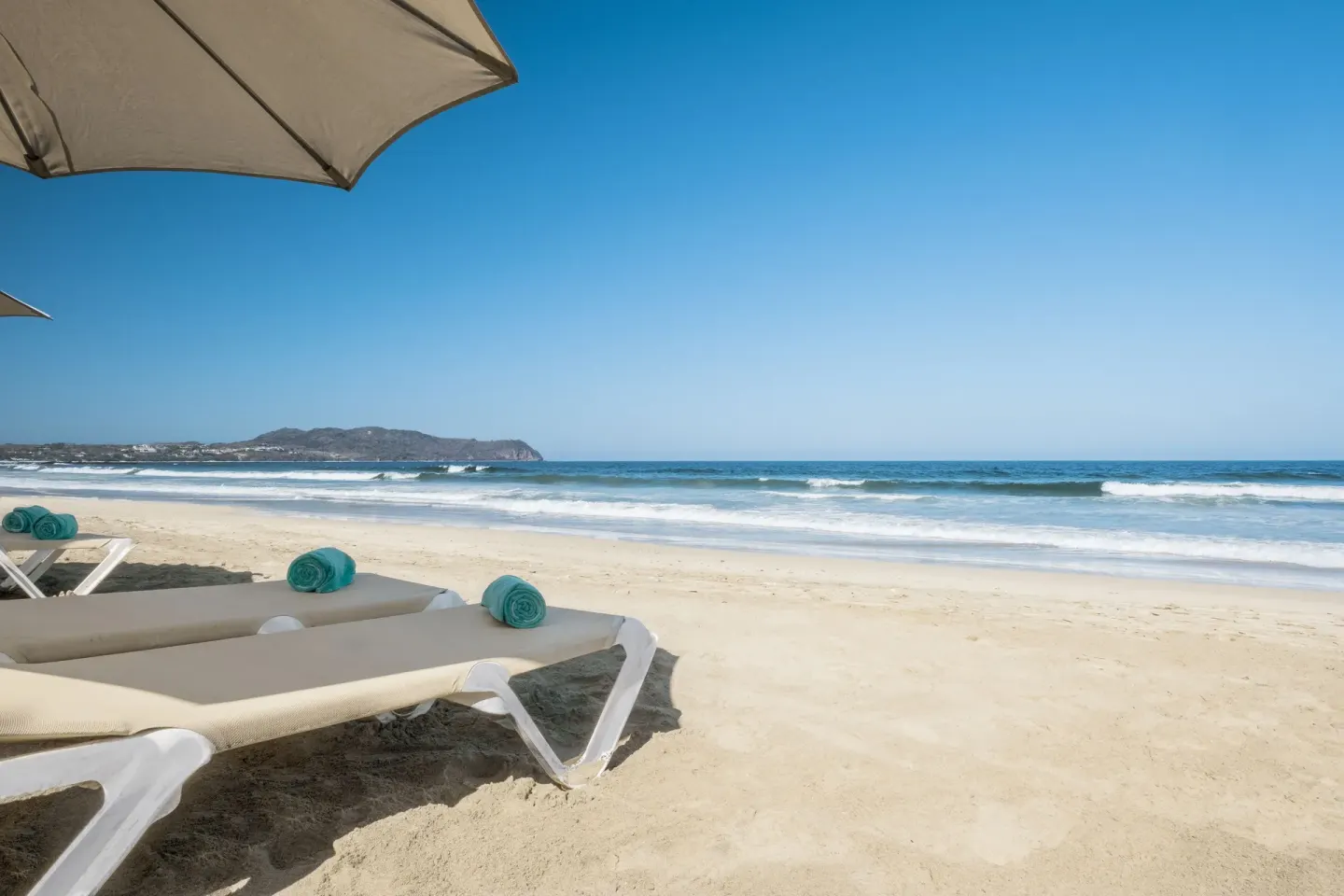 Beach loungers with turquoise towels facing the ocean at Iberostar Selection Playa Mita.