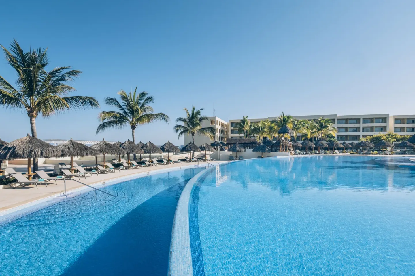 Curved main pool with palapas and resort buildings at Iberostar Selection Playa Mita.