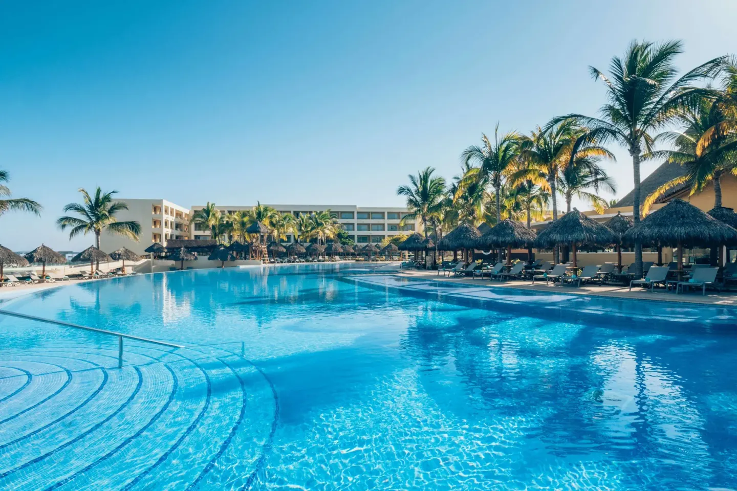 Large resort pool with palm trees and palapa loungers at Iberostar Selection Playa Mita.