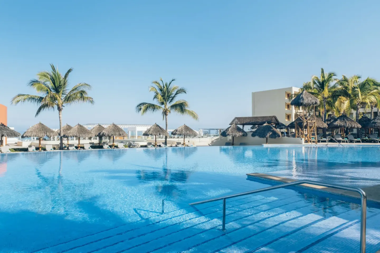 Main pool with palms, palapas, and ocean beyond at Iberostar Selection Playa Mita.