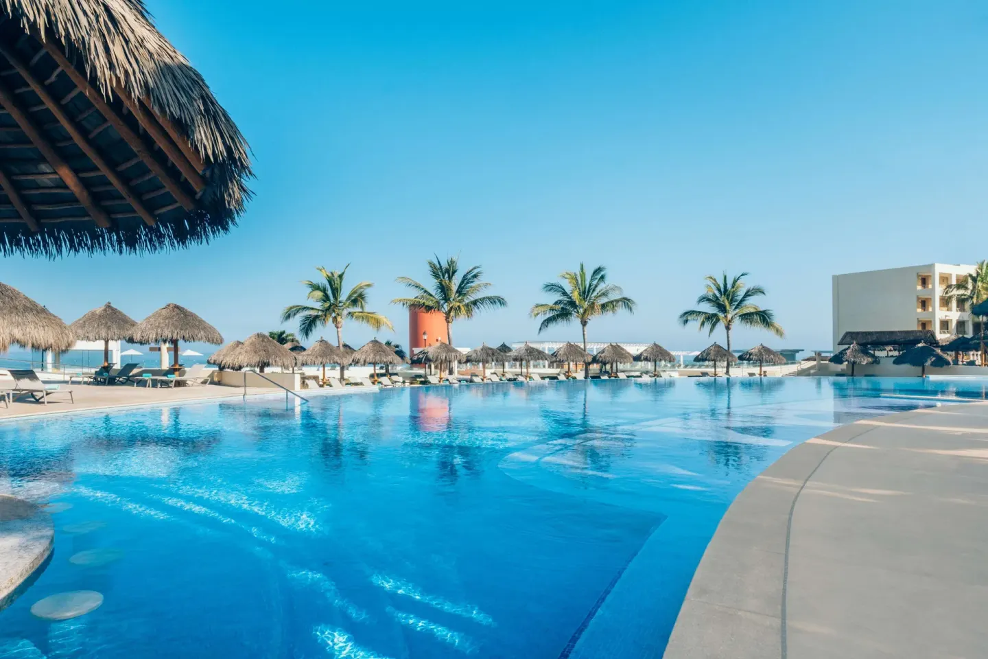 Pool deck with palapas, palms, and ocean views at Iberostar Selection Playa Mita.